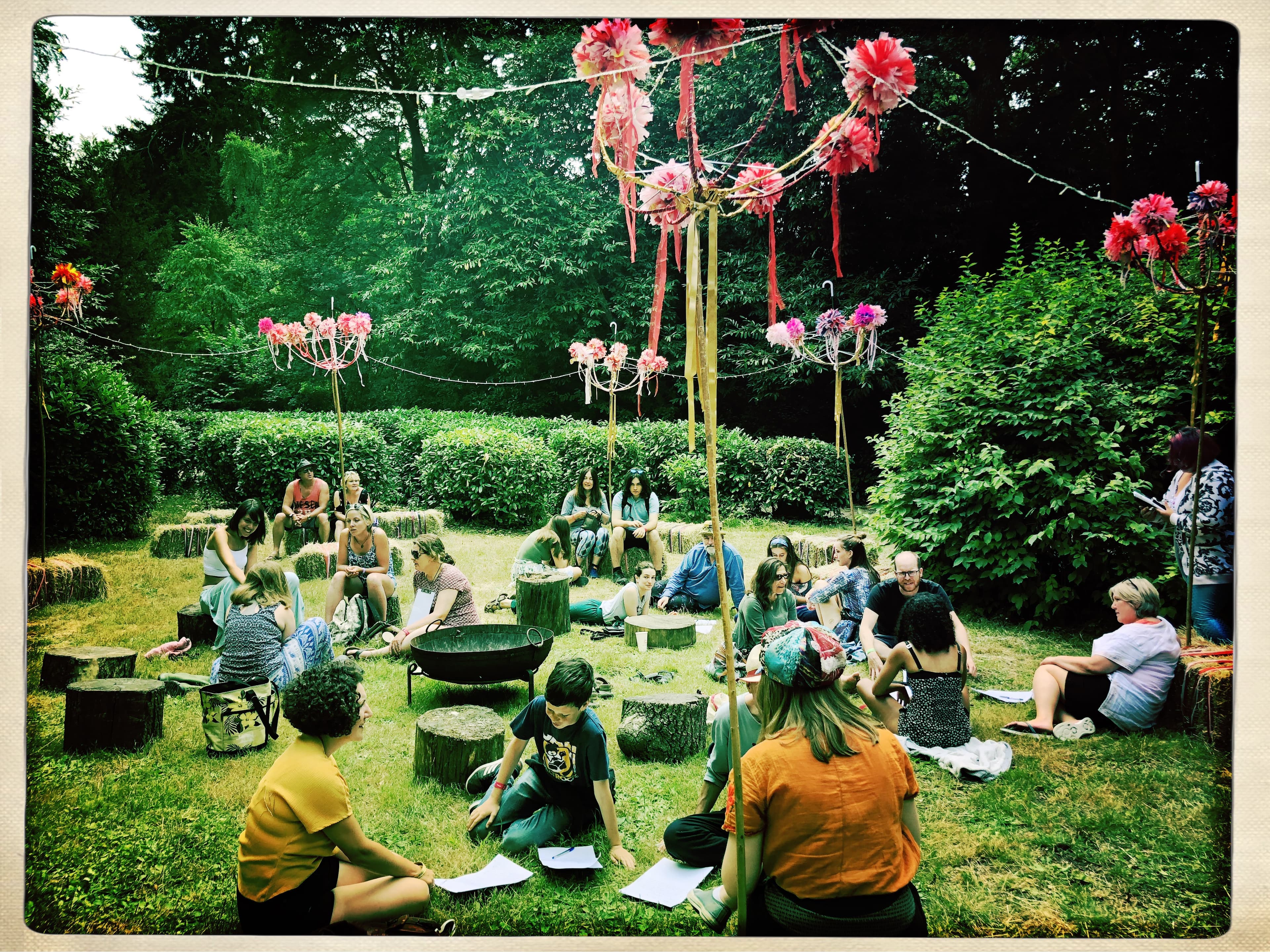 An image during the day of a fesitval field with fairylight hung in a circle from stakes to create a space to sit and relax. Decorated with ribbons and colourful accessories.